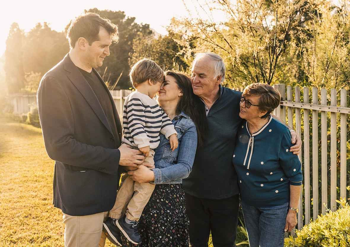 Familia de varias generaciones sonriendo junta al aire libre, capturada por un fotógrafo para familias en Mallorca.