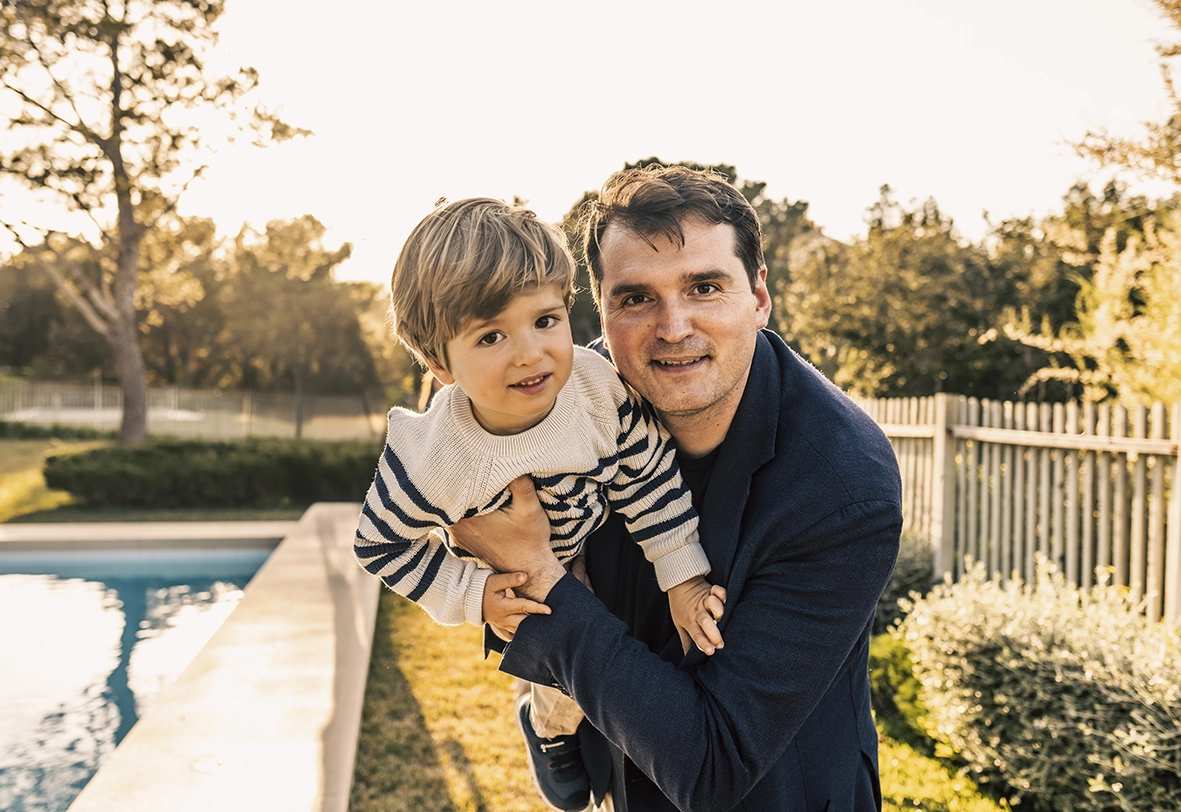 Padre sosteniendo a su hijo al aire libre junto a la piscina al atardecer, capturado por un fotógrafo para familias en Mallorca.