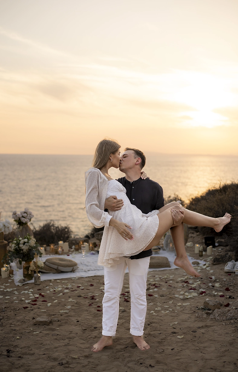 Groom holding his partner in his arms while kissing by the sea at sunset, captured by a photographer for proposals in Mallorca.