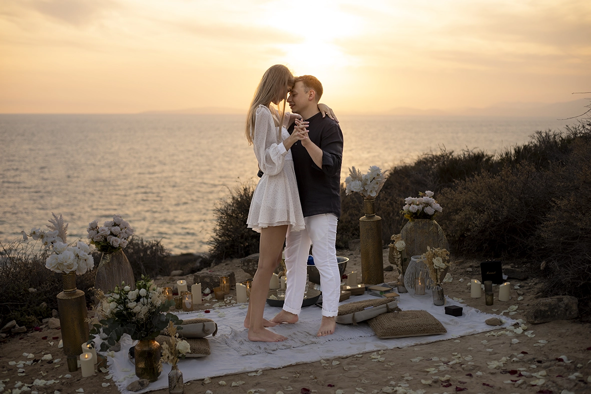 Couple standing on a blanket decorated with flowers and candles, enjoying their proposal in Mallorca at sunset. Captured by a photographer for proposals in Mallorca.