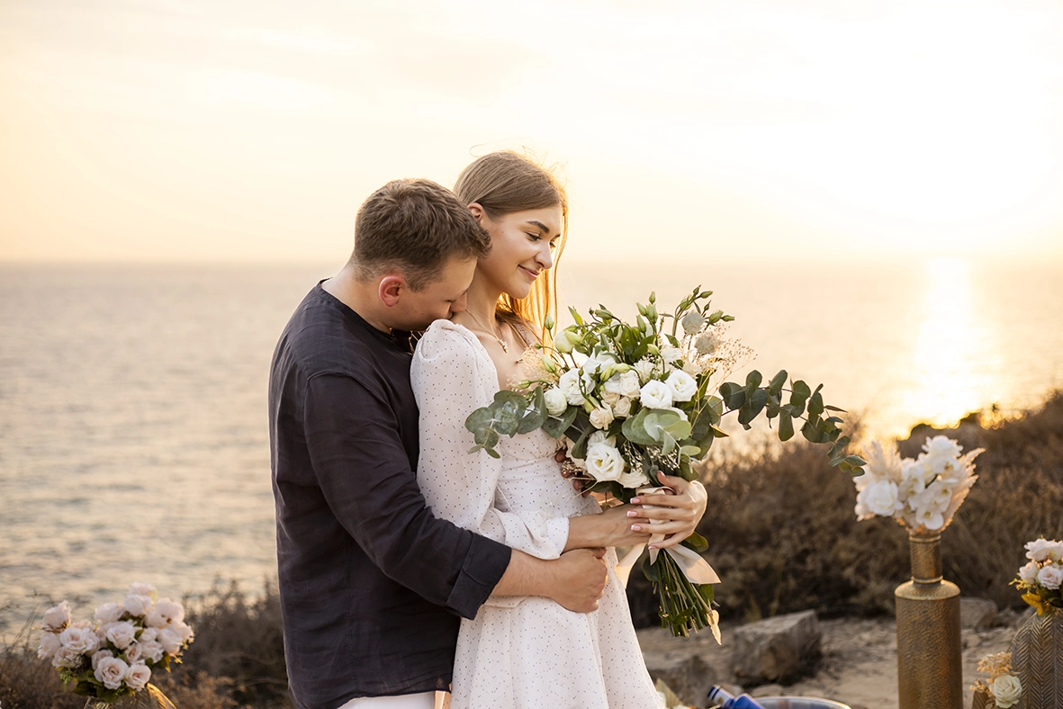 Groom embracing his partner while she holds a bouquet of flowers during their proposal in Mallorca at sunset. Captured by a photographer for proposals in Mallorca.