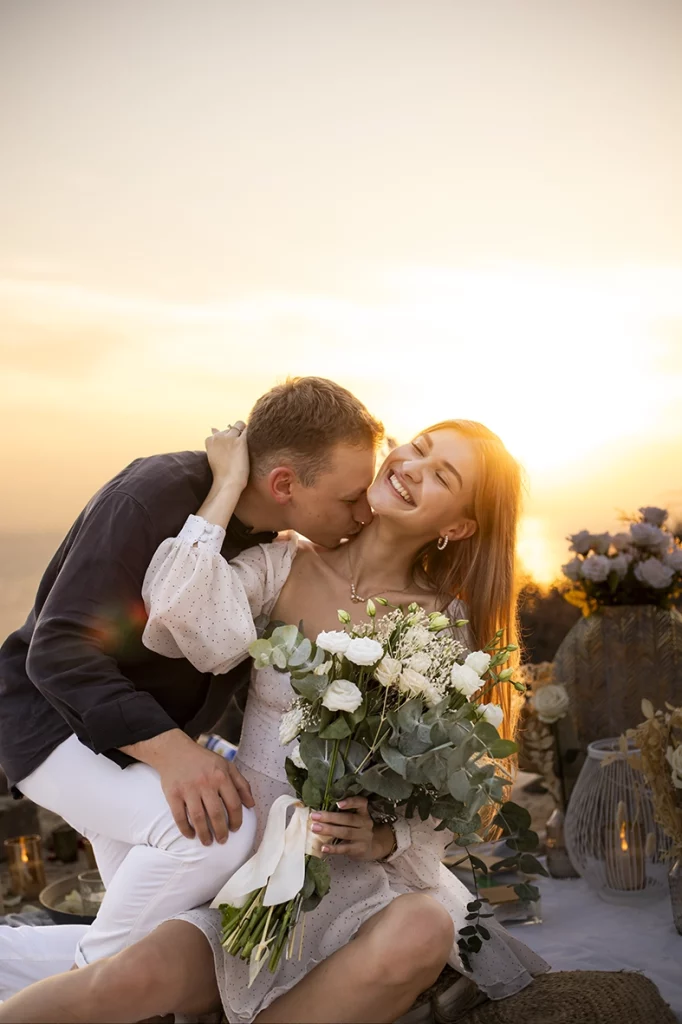 Novio besando a su pareja al atardecer con ramo de flores durante su pedida de mano en Mallorca, captado por un fotógrafo para pedida de mano en Mallorca.