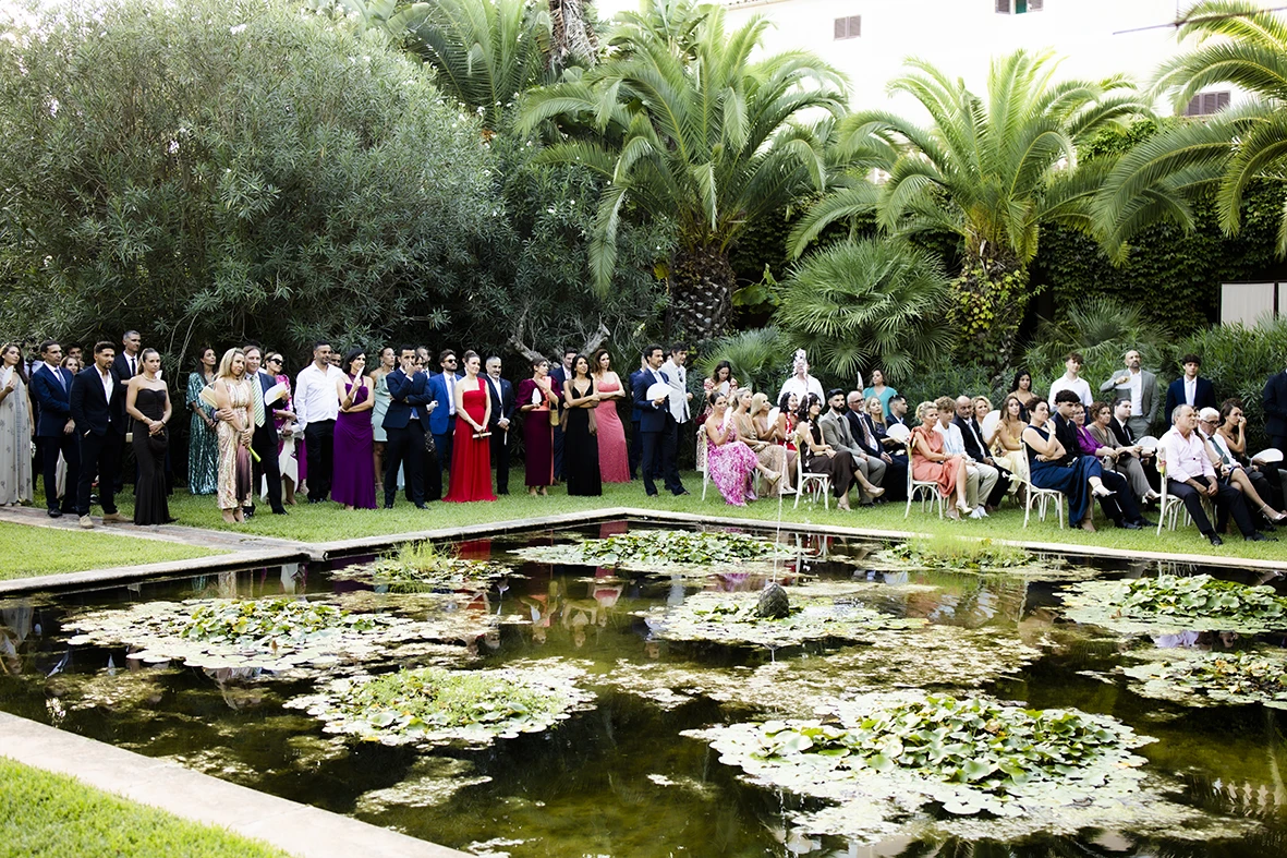 Outdoor wedding ceremony by a pond with flowers and palm trees in Mallorca – Wedding photographer in Mallorca – Inma del Valle –