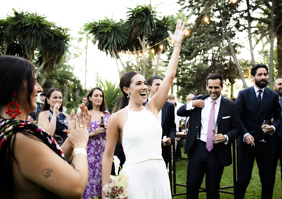 Smiling bride raising her arm while entering among guests during a wedding in Mallorca – Wedding photographer in Mallorca – Inma del Valle –