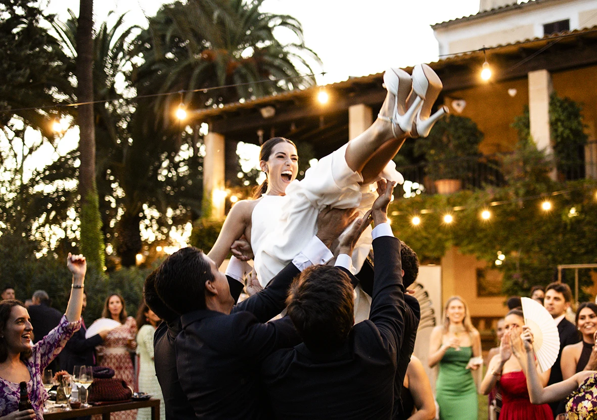 Bride being lifted into the air by guests during a lively wedding celebration in Mallorca.