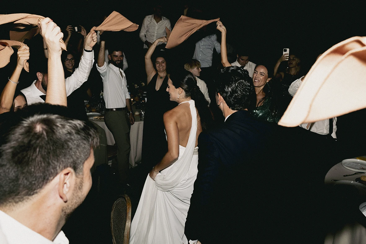 Bride in a white dress dancing while guests celebrate waving napkins during a Mallorca wedding.