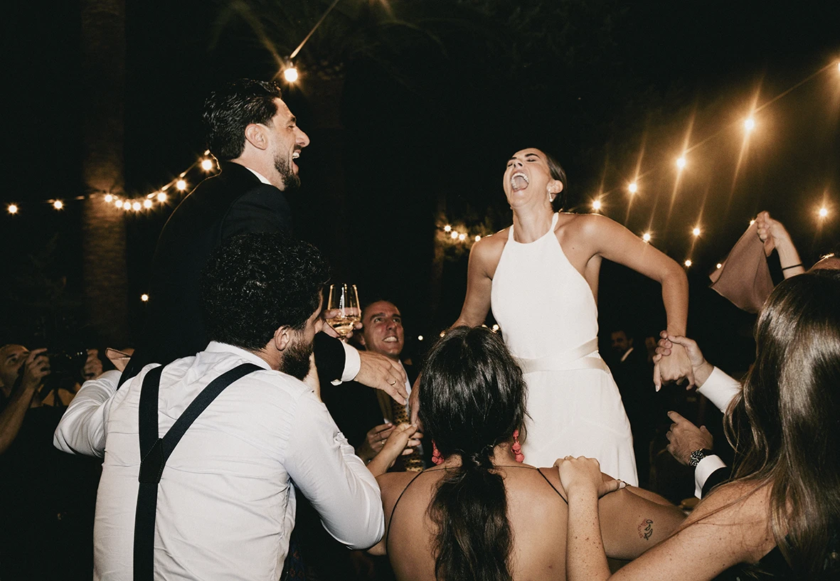 Bride laughing with joy while being lifted during her wedding party in Mallorca.