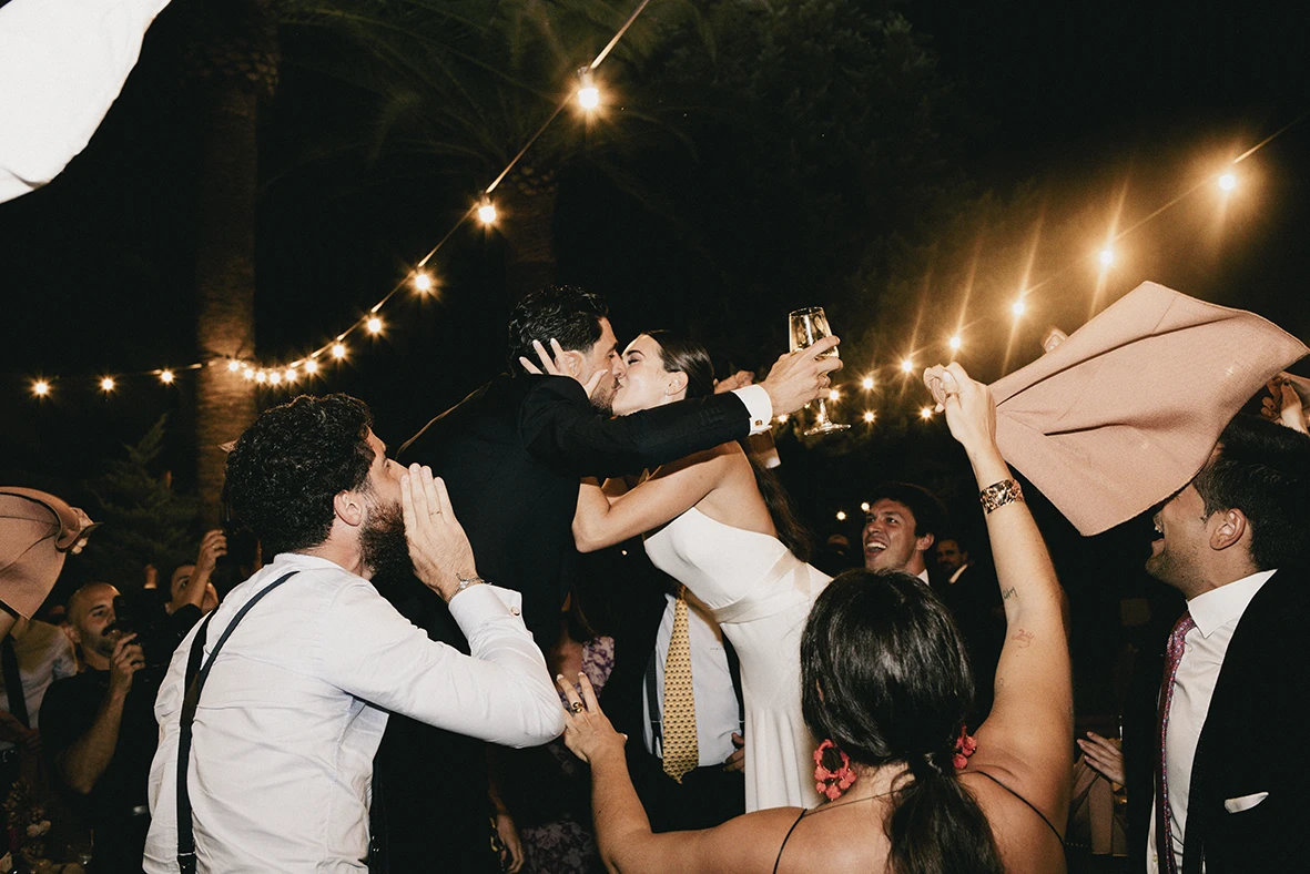 Bride and groom kissing while guests celebrate during their wedding party in Mallorca.