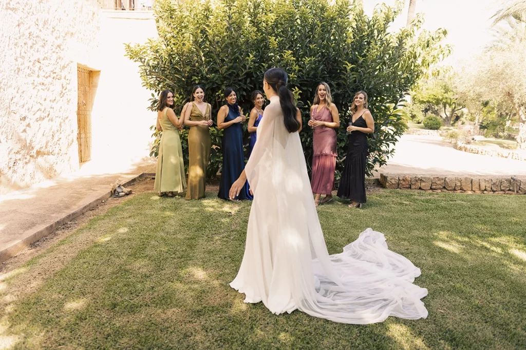 The bride seen from behind in her white dress walking towards her colorful bridesmaids under the shade of a tree – Wedding photographer in Mallorca – Inma del Valle -