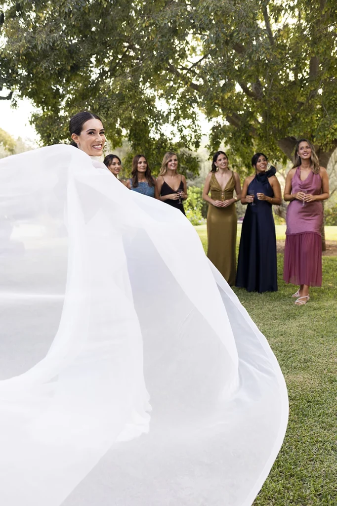 The bride’s veil flowing in the wind as the bridesmaids smile in the background – Wedding photographer in Mallorca – Inma del Valle -