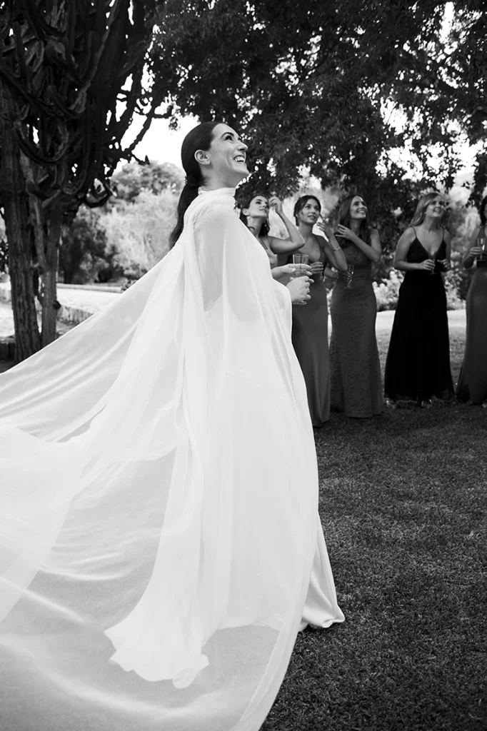 Smiling bride spinning with her dress flowing in the wind, surrounded by guests – Wedding photographer in Mallorca – Inma del Valle -