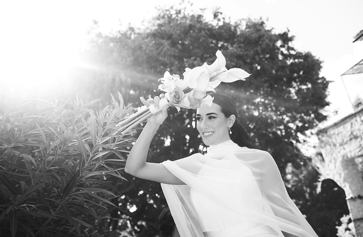 The bride smiles while raising her bouquet, lit by a strong backlight – Wedding photographer in Mallorca – Inma del Valle -