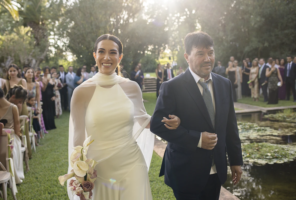 The bride enters smiling, arm in arm with her father – Wedding photographer in Mallorca – Inma del Valle -