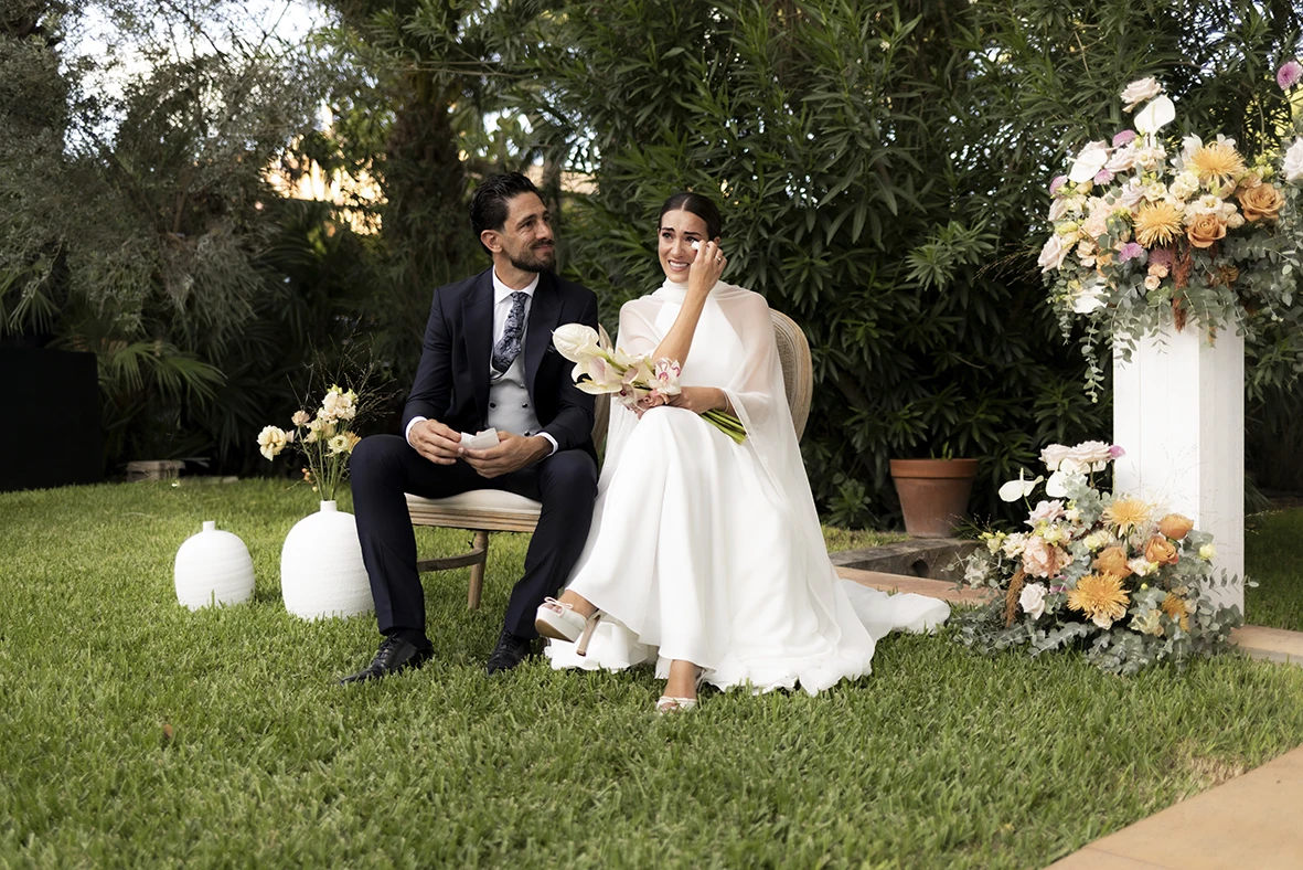 Bride and groom seated surrounded by flowers during the ceremony at Finca Santa Cirga – Wedding photographer in Mallorca – Inma del Valle -