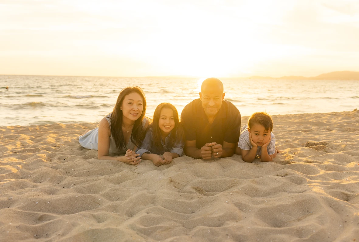 Family lying on the sand facing the sea during sunset in Mallorca. Photo taken by Inma del Valle, photographer in Mallorca.