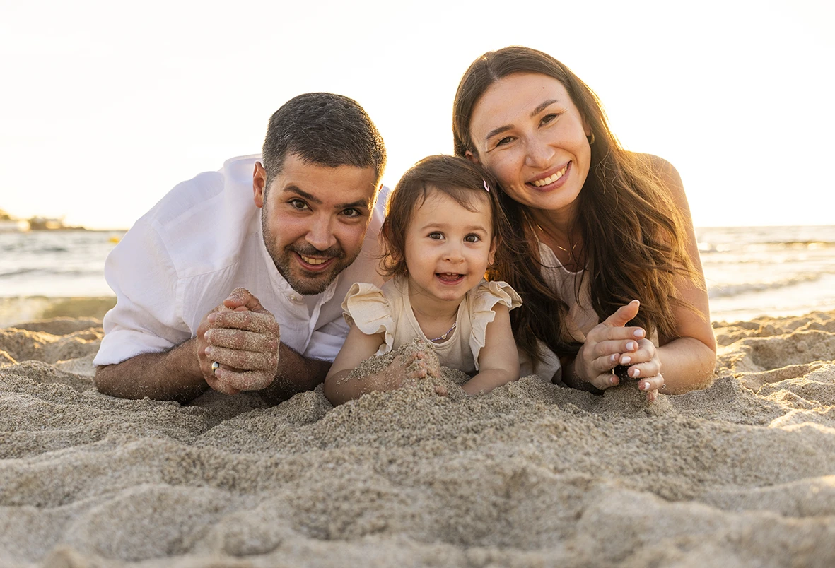 Familia tumbada sobre la arena sonriendo durante una sesión con fotógrafo en Mallorca