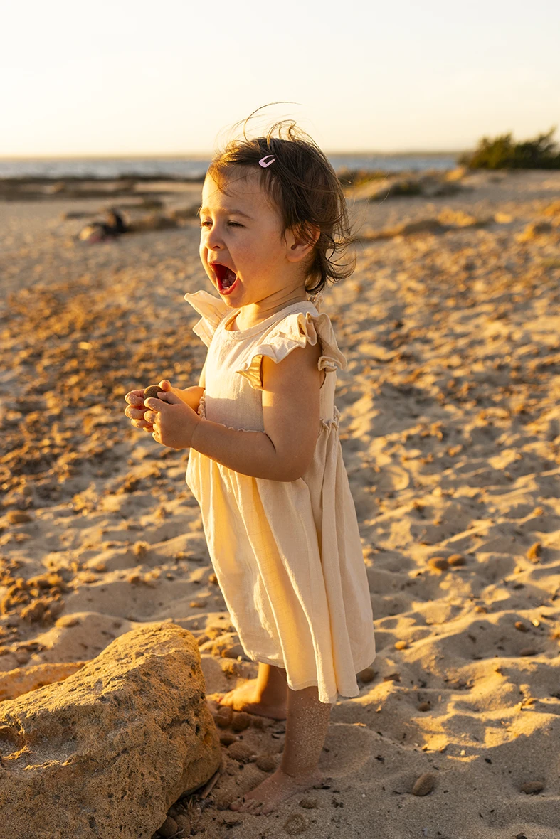 Niña sonriendo y jugando en la arena durante una sesión de fotografía de familias en Mallorca al atardecer