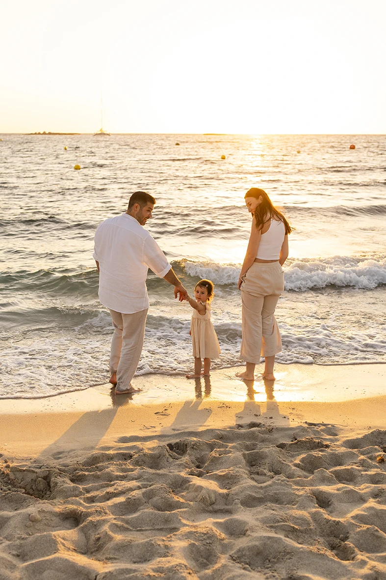 Padres jugando con su hija en la orilla del mar durante una sesión de fotografía de familias en Mallorca al atardecer