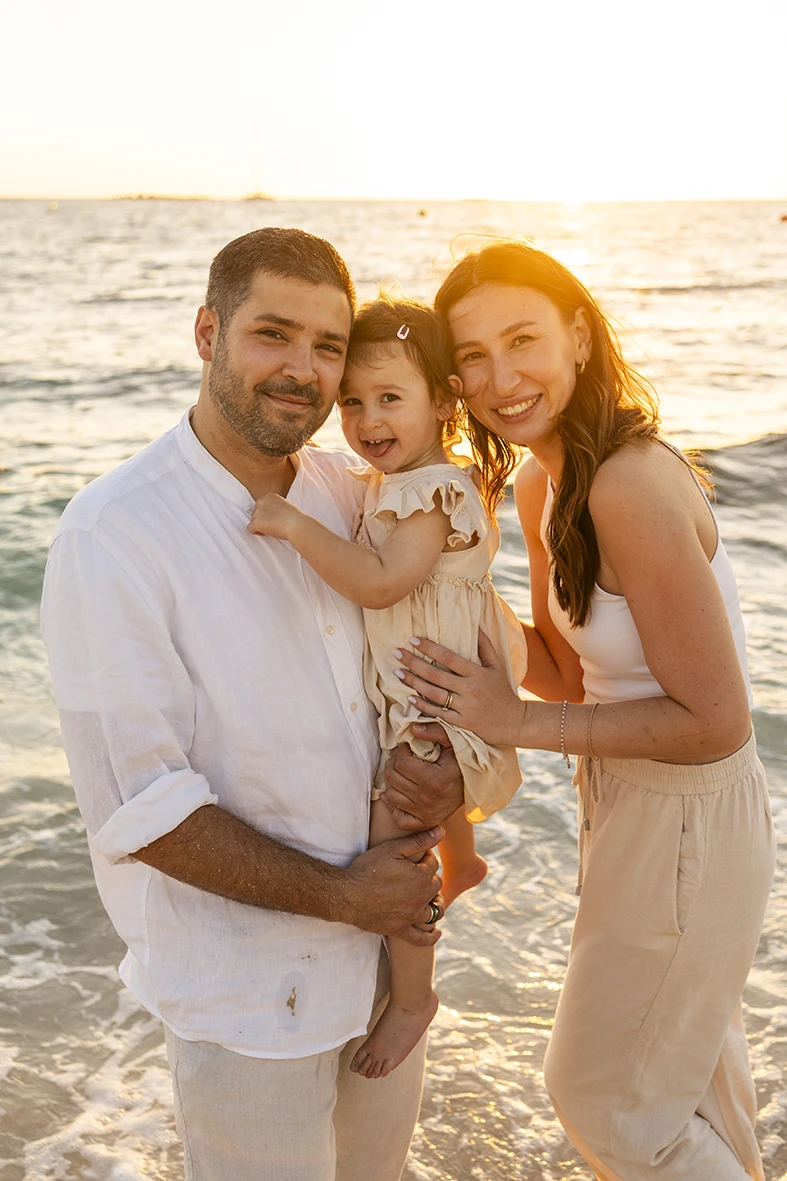 Familia abrazada y sonriendo frente al mar al atardecer durante una sesión con fotógrafo en Mallorca