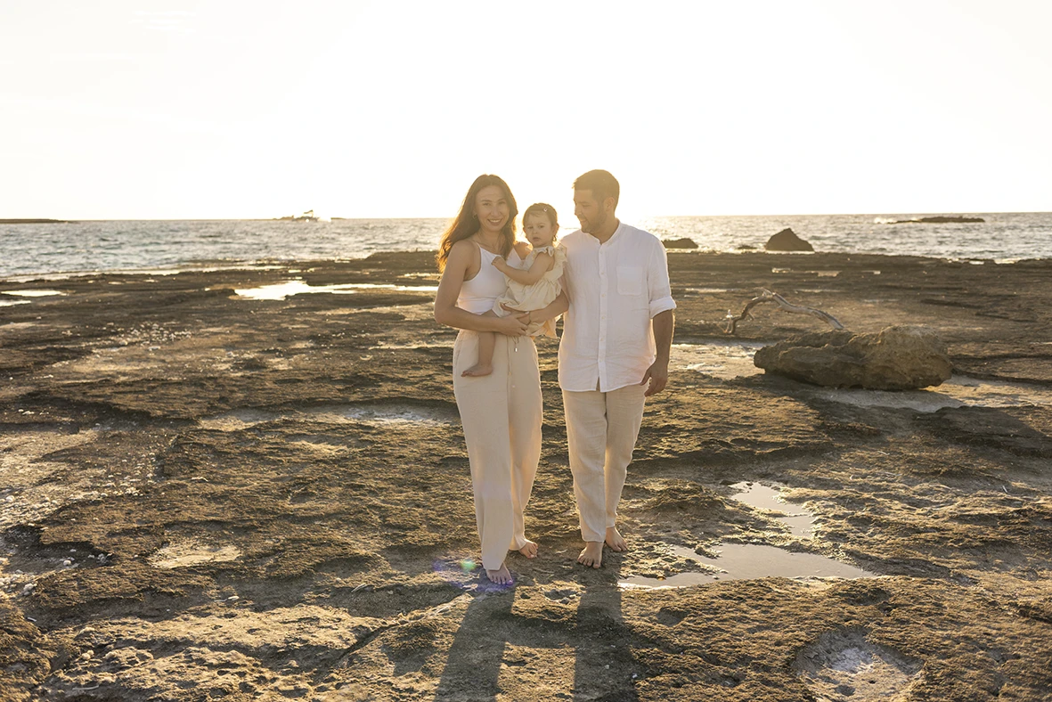 Familia caminando sobre las rocas junto al mar al atardecer durante una sesión de fotografía de familias en Mallorca