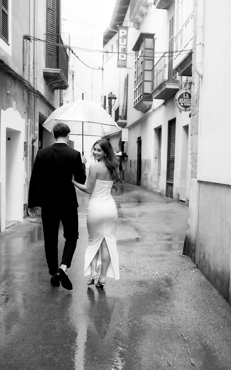 Daiana y Noah caminan bajo la lluvia tomados de la mano durante su fotografía de pareja en Mallorca