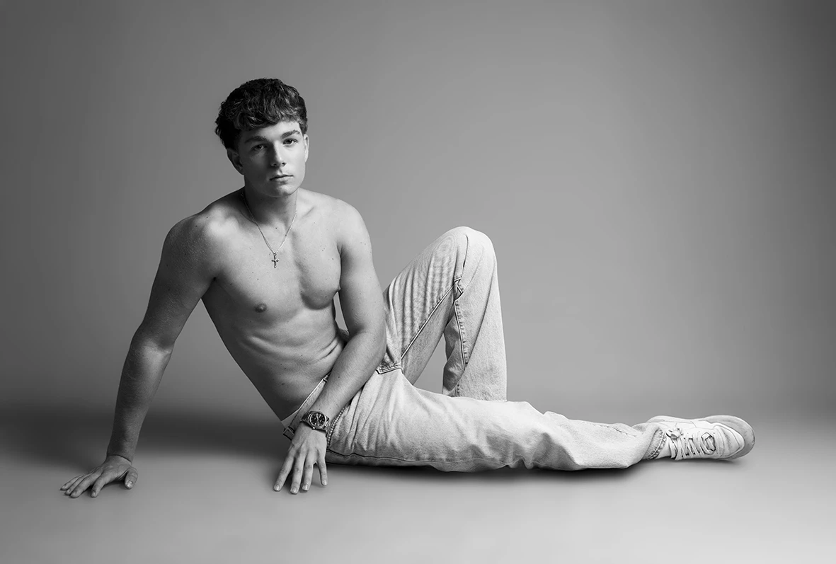 Modelo masculino recostado en el suelo en pose relajada durante sesión en blanco y negro.
