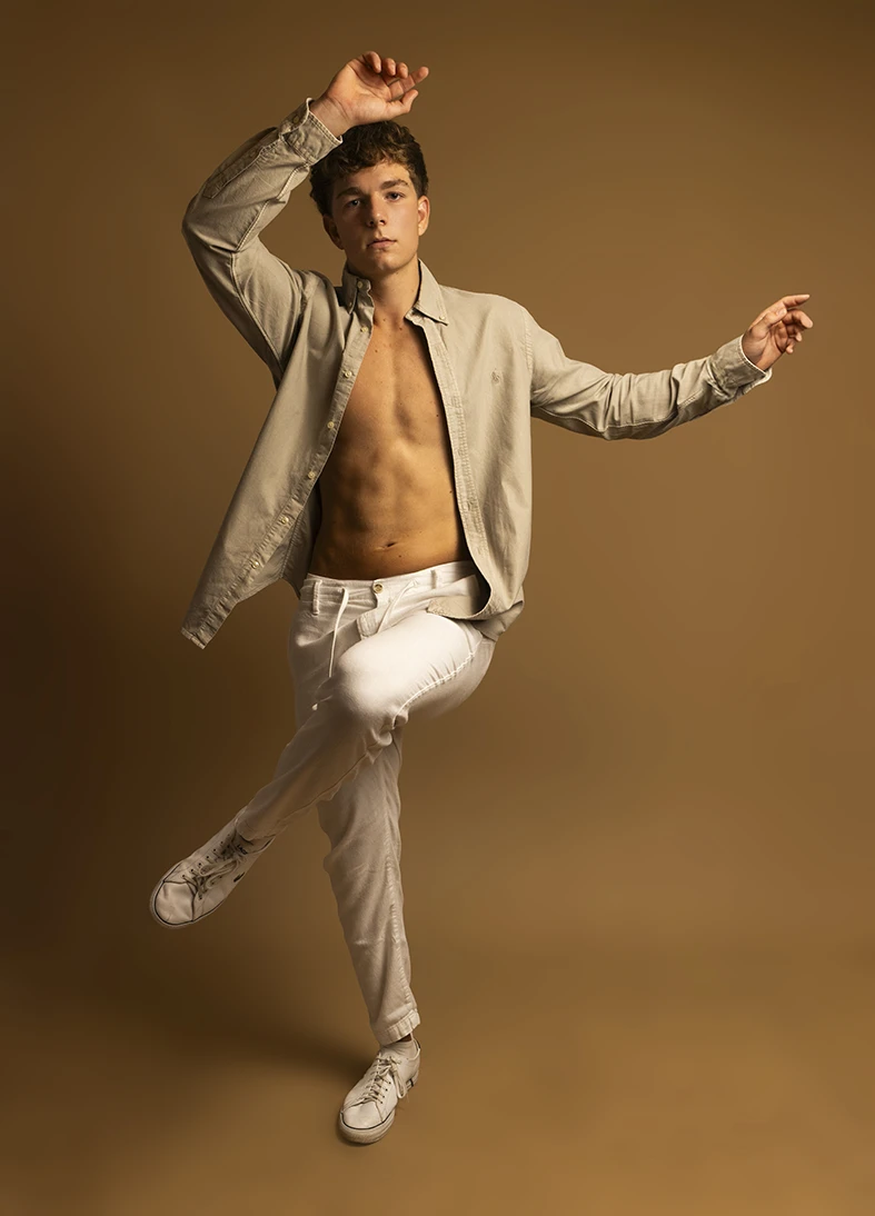 Male model jumps mid-air during studio session with beige background.