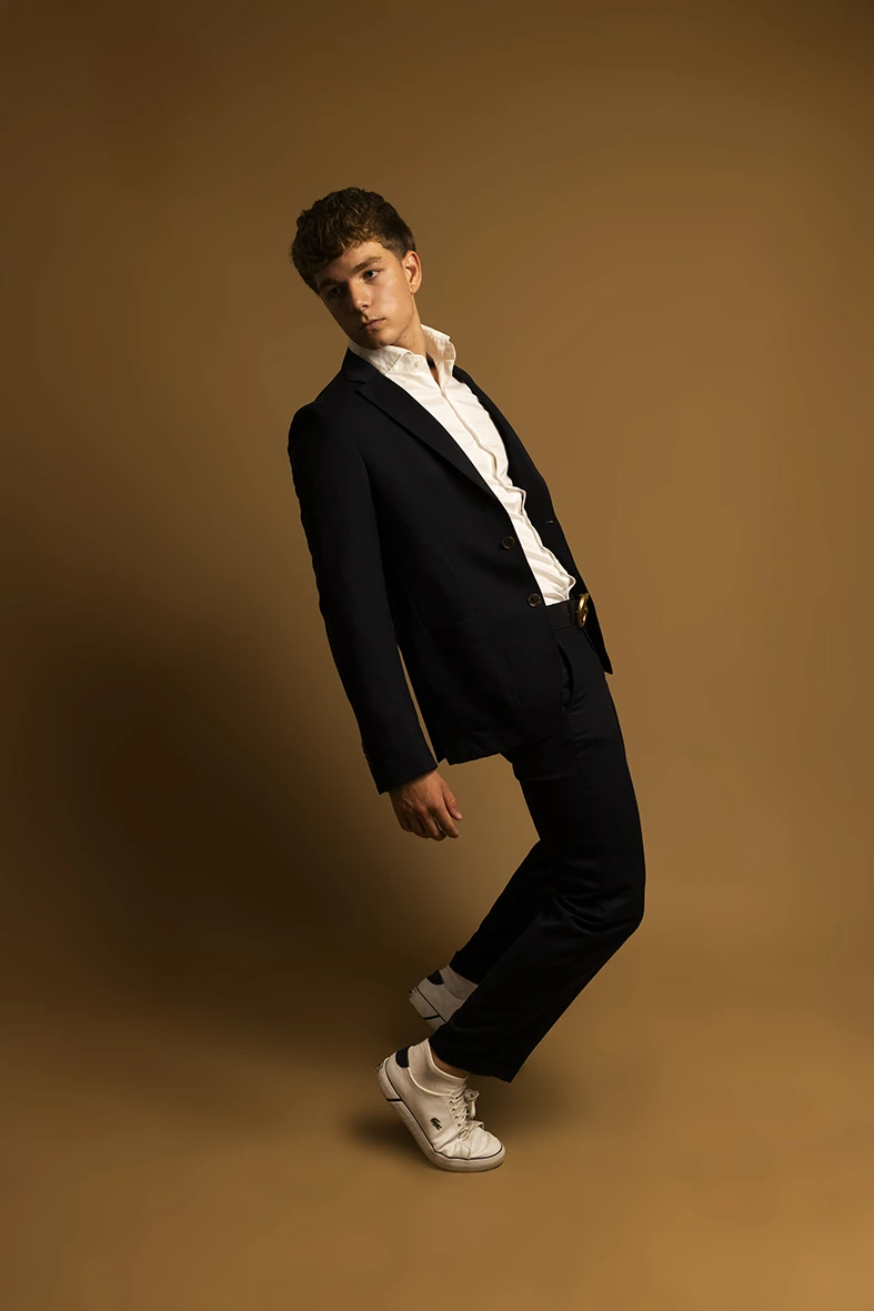 Male model in black suit leaning back during studio photoshoot.