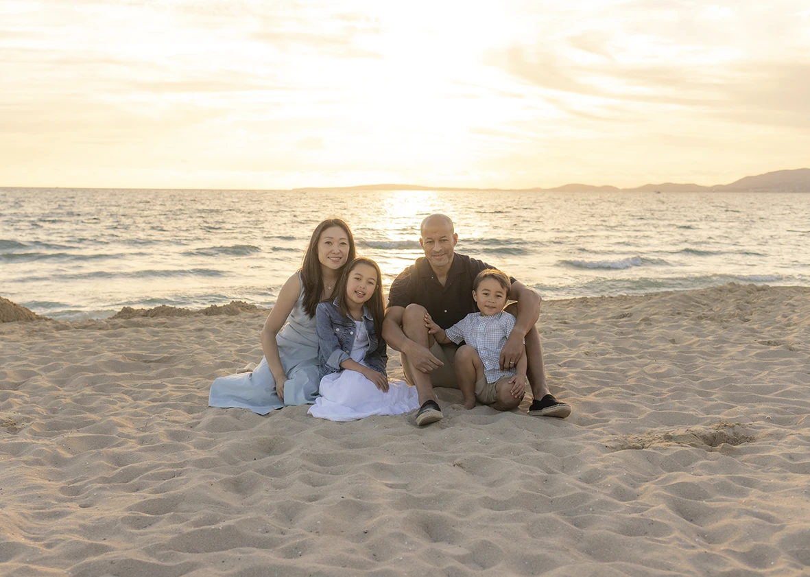 Familia sentada en la arena al atardecer durante sesión de fotos con Inma del Valle en Mallorca.
