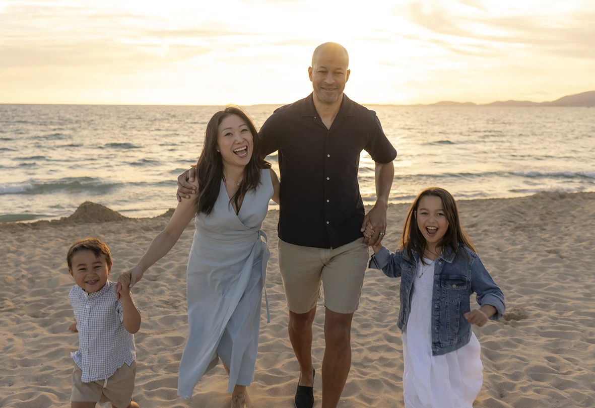 Familia corriendo y sonriendo en la playa al atardecer durante sesión con Inma del Valle en Mallorca.