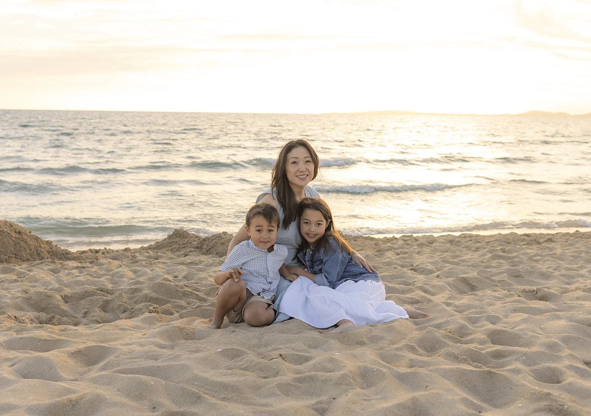 Madre con sus dos hijos sentados en la arena frente al mar durante sesión con Inma del Valle en Mallorca.