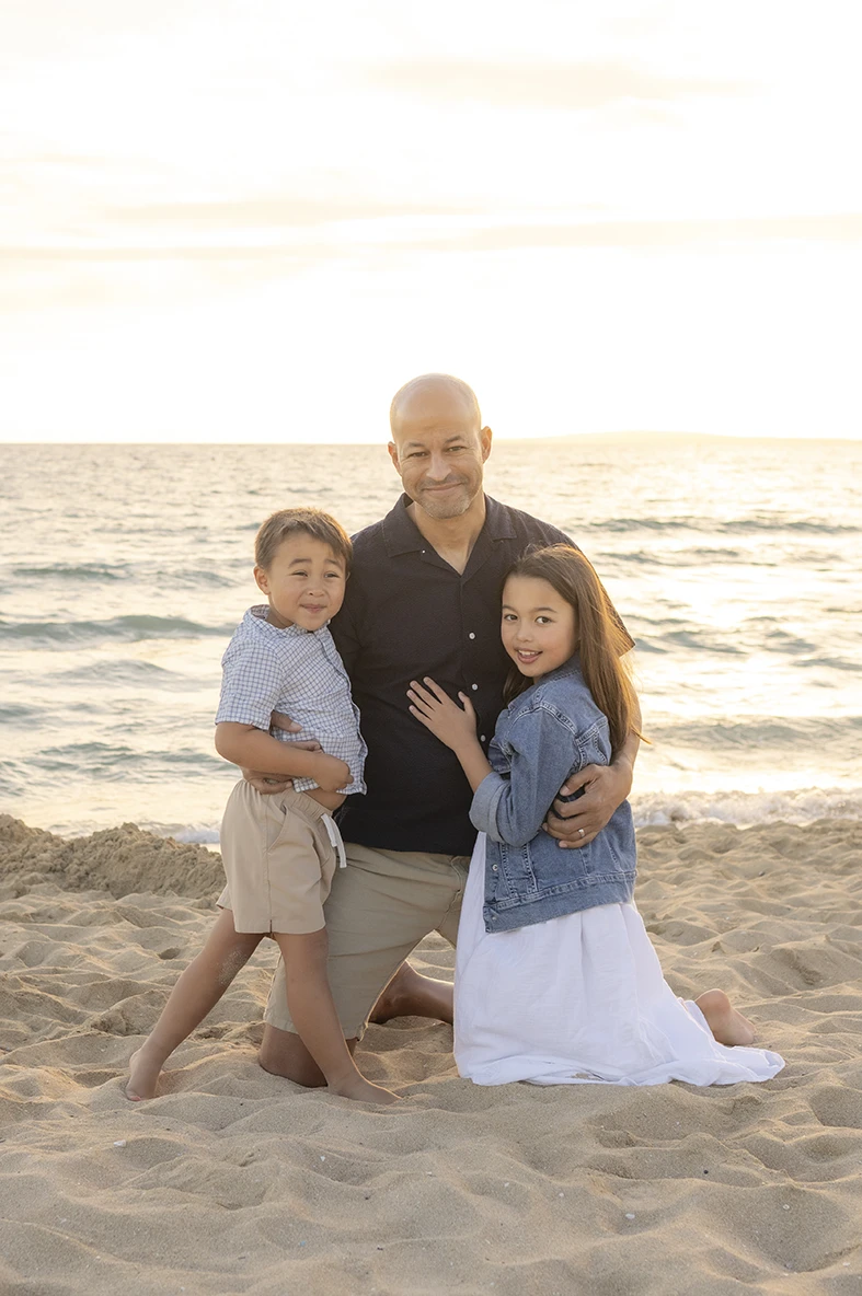 Padre abrazando a sus dos hijos durante sesión de fotos al atardecer en la playa con Inma del Valle en Mallorca.
