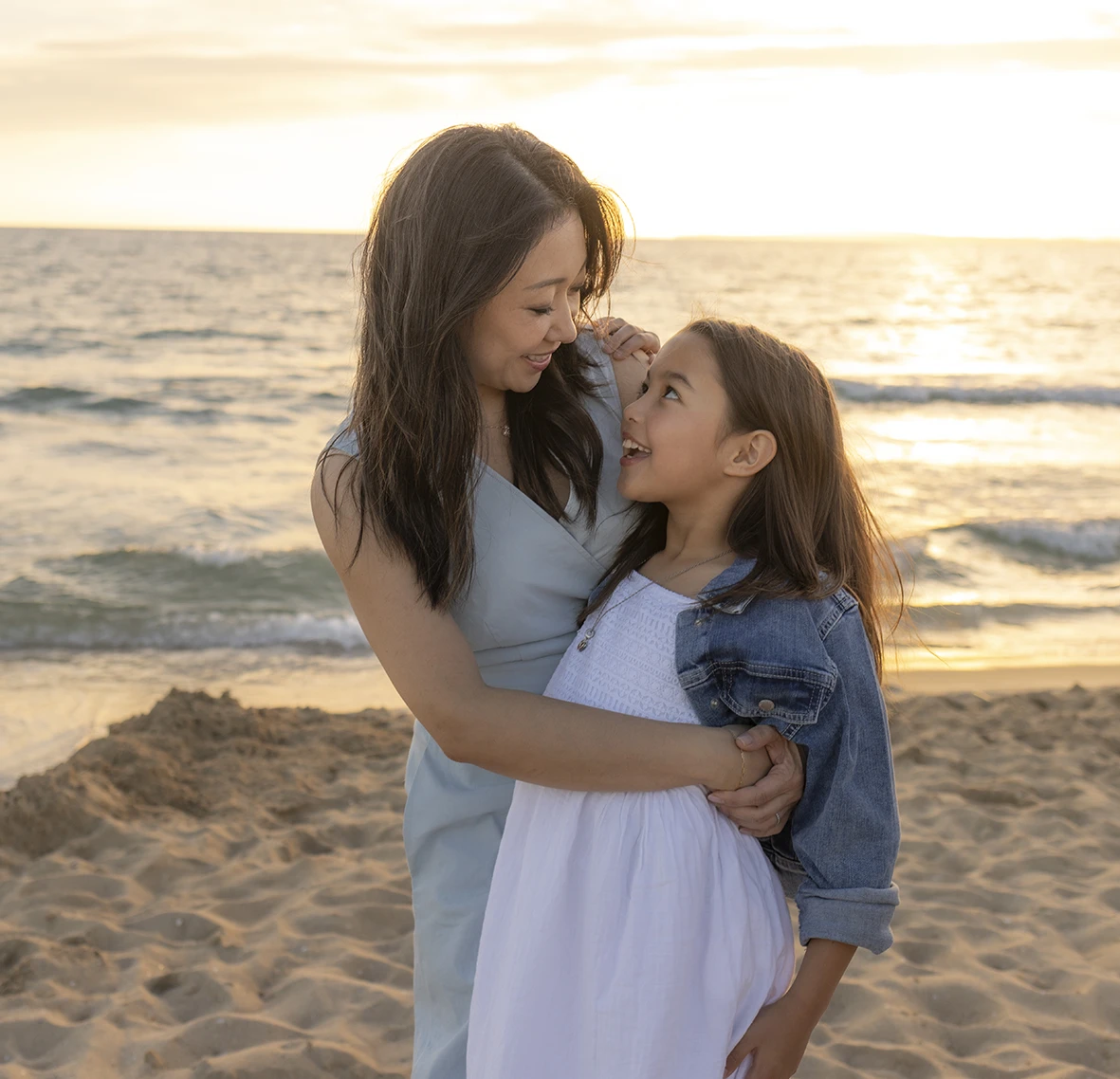 Madre e hija abrazadas mirando con ternura en la playa durante el atardecer con Inma del Valle en Mallorca.