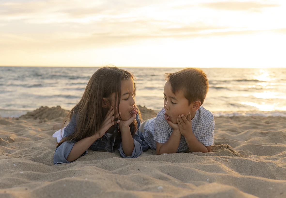 Hermanos tumbados en la arena al atardecer conversando durante sesión de fotos con Inma del Valle en Mallorca.