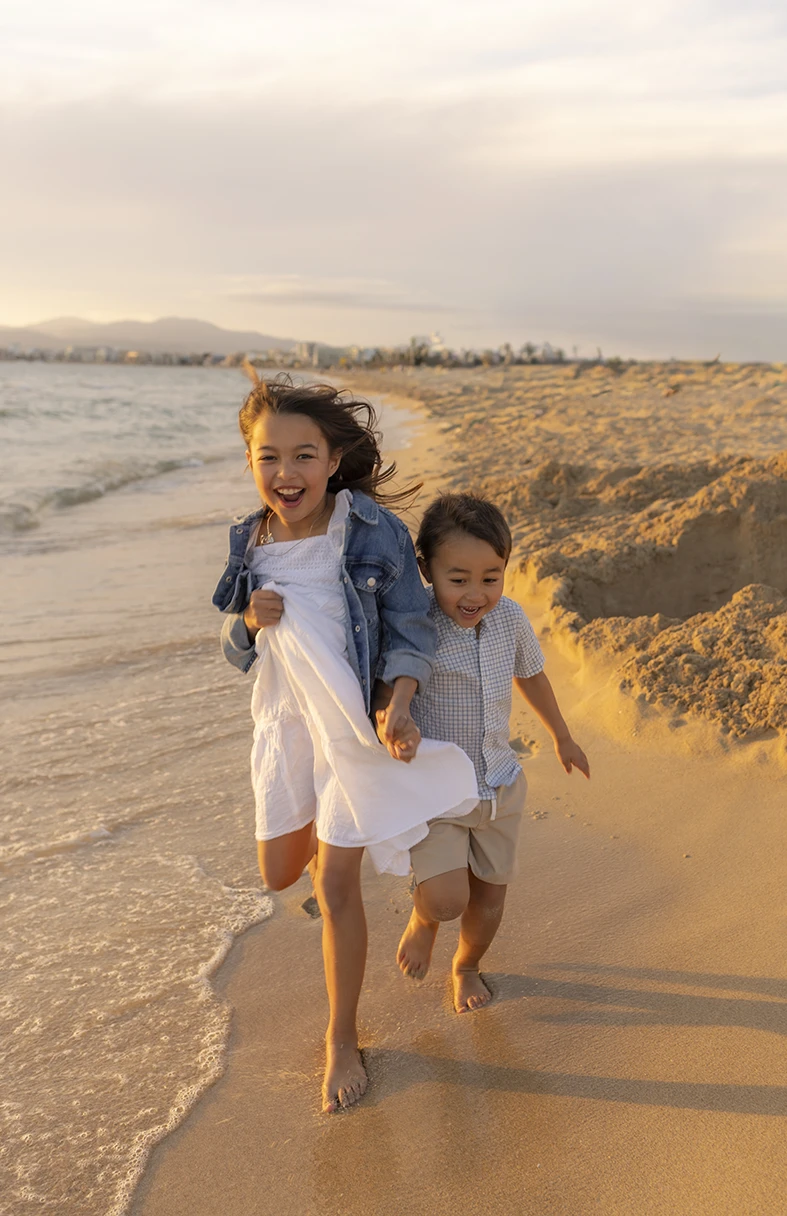 Hermanos corriendo junto al mar al atardecer durante sesión de fotos con Inma del Valle en Mallorca.