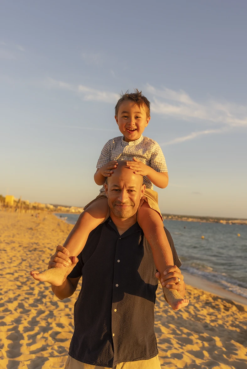 Niño feliz sobre los hombros de su padre en la playa al atardecer en Mallorca con Inma del Valle.
