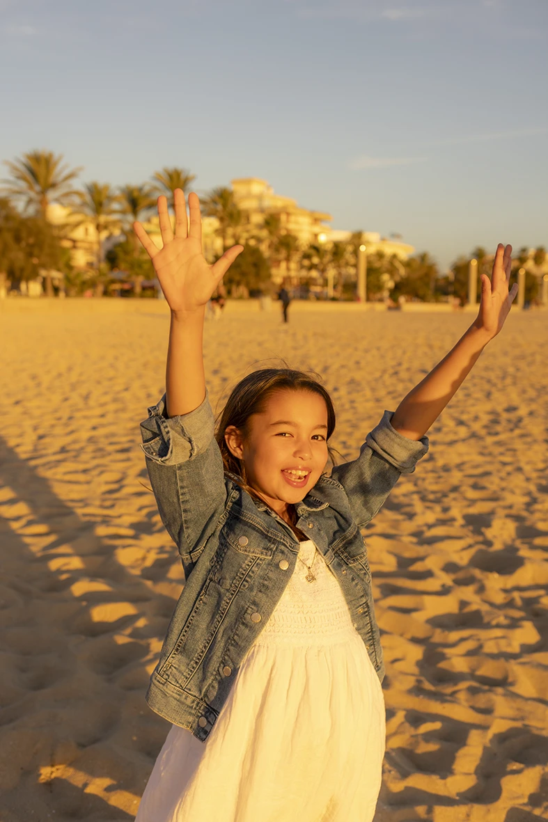 Niña levantando los brazos con alegría en la playa al atardecer en Mallorca, capturada por Inma del Valle.