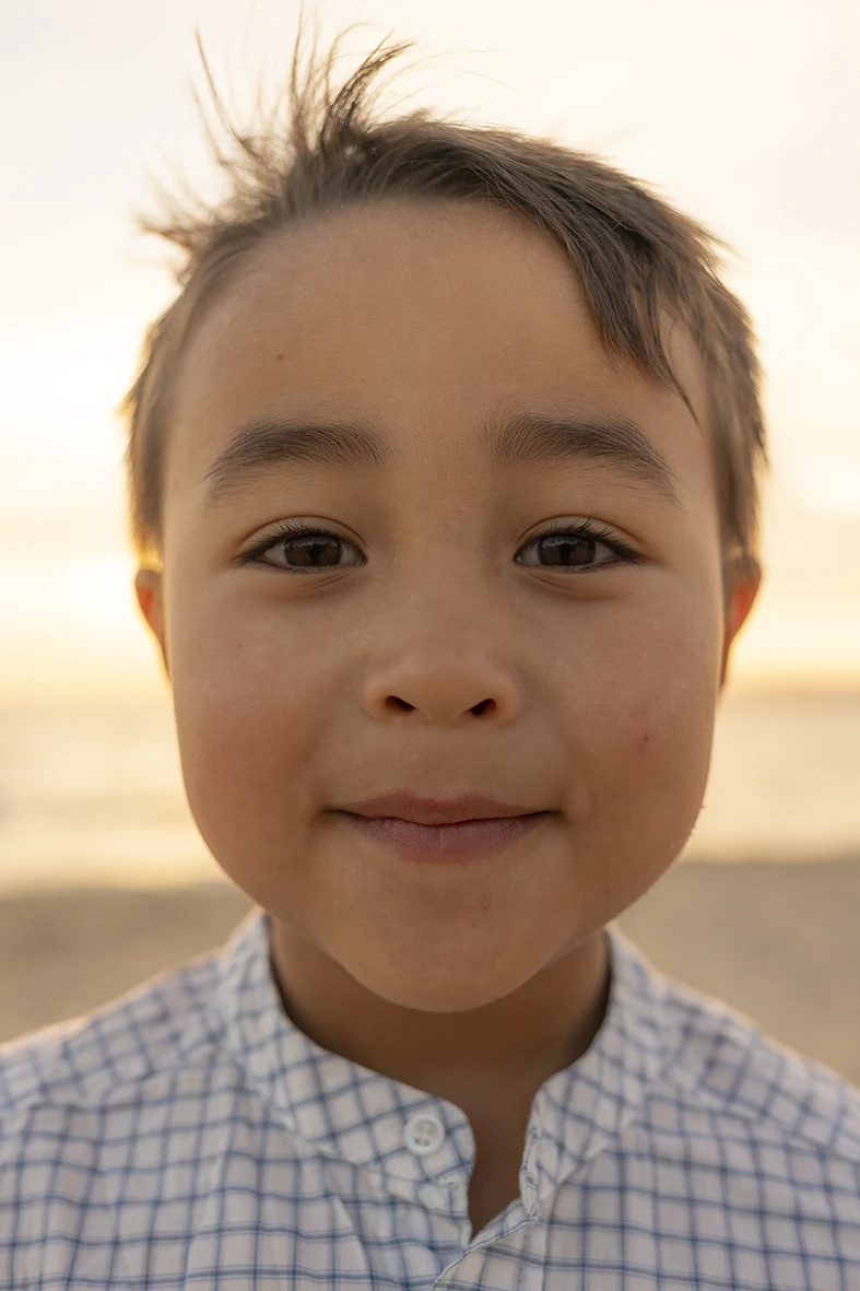 Niño mirando a cámara con una expresión tranquila durante una sesión de fotos familiar en la playa al atardecer, realizada por la fotógrafa Inma del Valle en Mallorca.