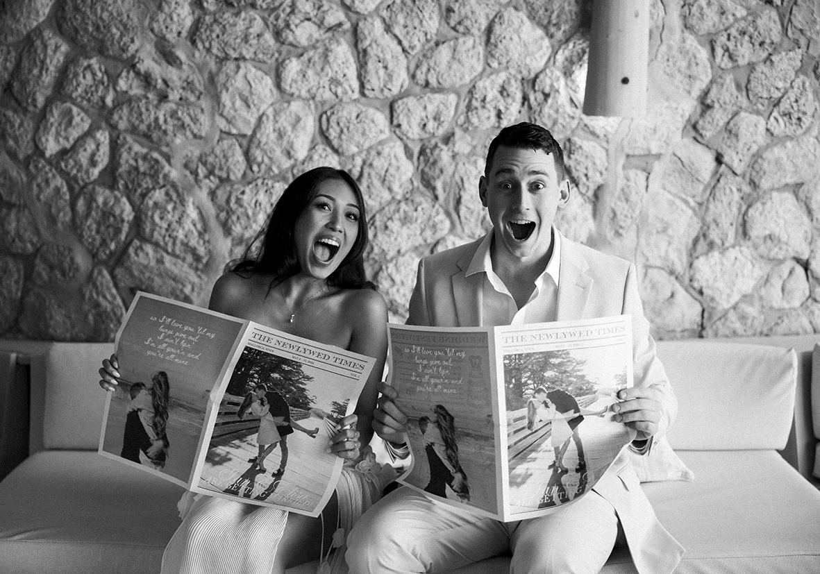 Pareja divertida leyendo revistas antes de su boda de varios días en Mallorca.