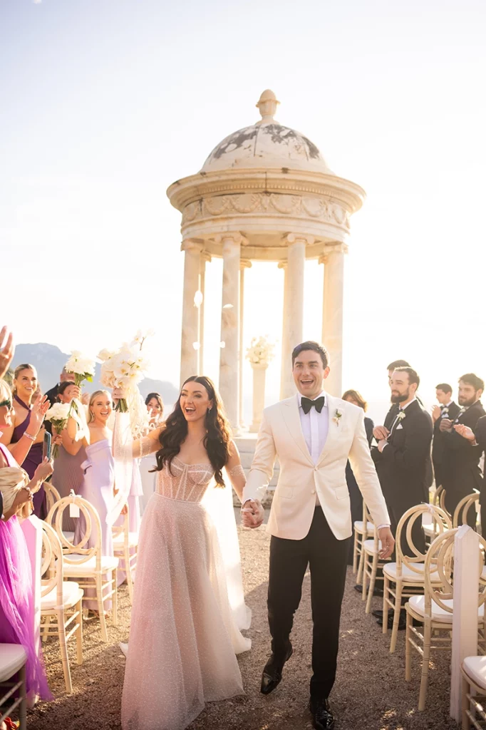 Bride and groom celebrating with guests in front of Son Marroig temple at sunset