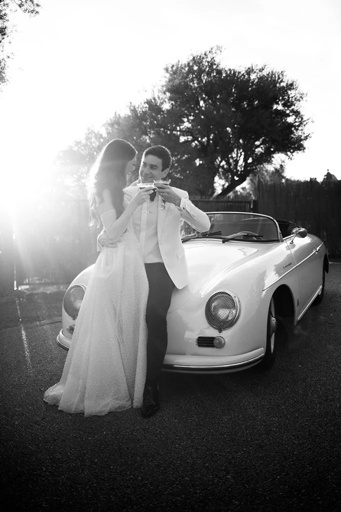 Bride and groom toasting beside classic white convertible at Son Marroig wedding in Mallorca