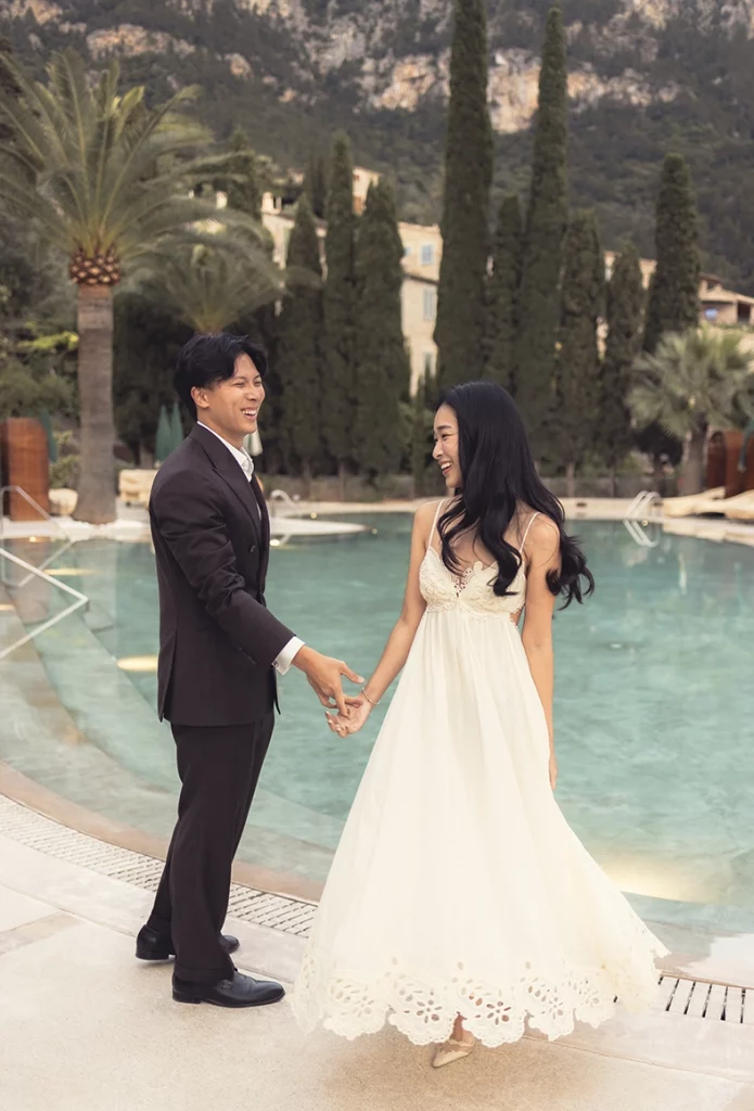 Pareja feliz cogida de la mano junto a la piscina después de una pedida de mano en Belmond La Residencia Deià