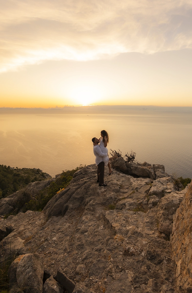 Pareja abrazándose sobre los acantilados de Mallorca durante el atardecer después de una pedida de mano sorpresa fotografiada por Inma del Valle