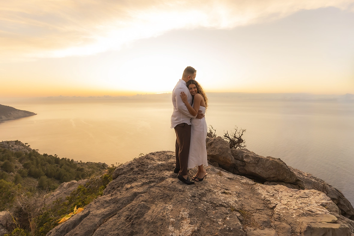 Pareja abrazándose al atardecer en un acantilado de Mallorca después de una pedida de mano sorpresa fotografiada por Inma del Valle.