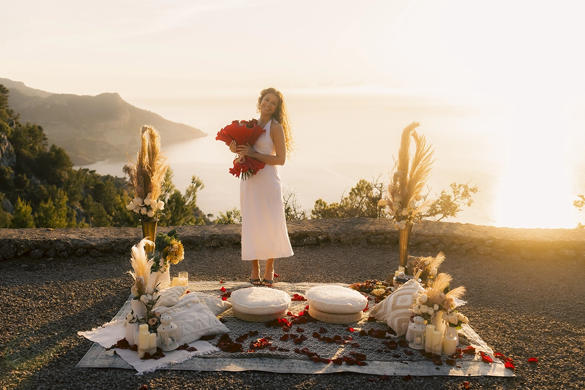 Mujer celebrando su pedida de mano sorpresa en Mallorca con un ramo de rosas rojas y una decoración romántica de lujo al atardecer, fotografiada por Inma del Valle.