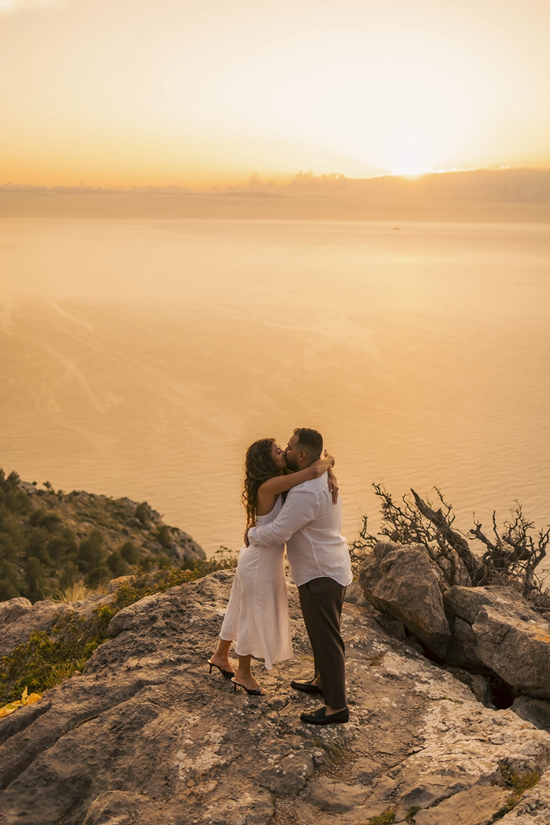 Pareja besándose sobre los acantilados de Mallorca durante el atardecer después de una pedida de mano sorpresa fotografiada por Inma del Valle