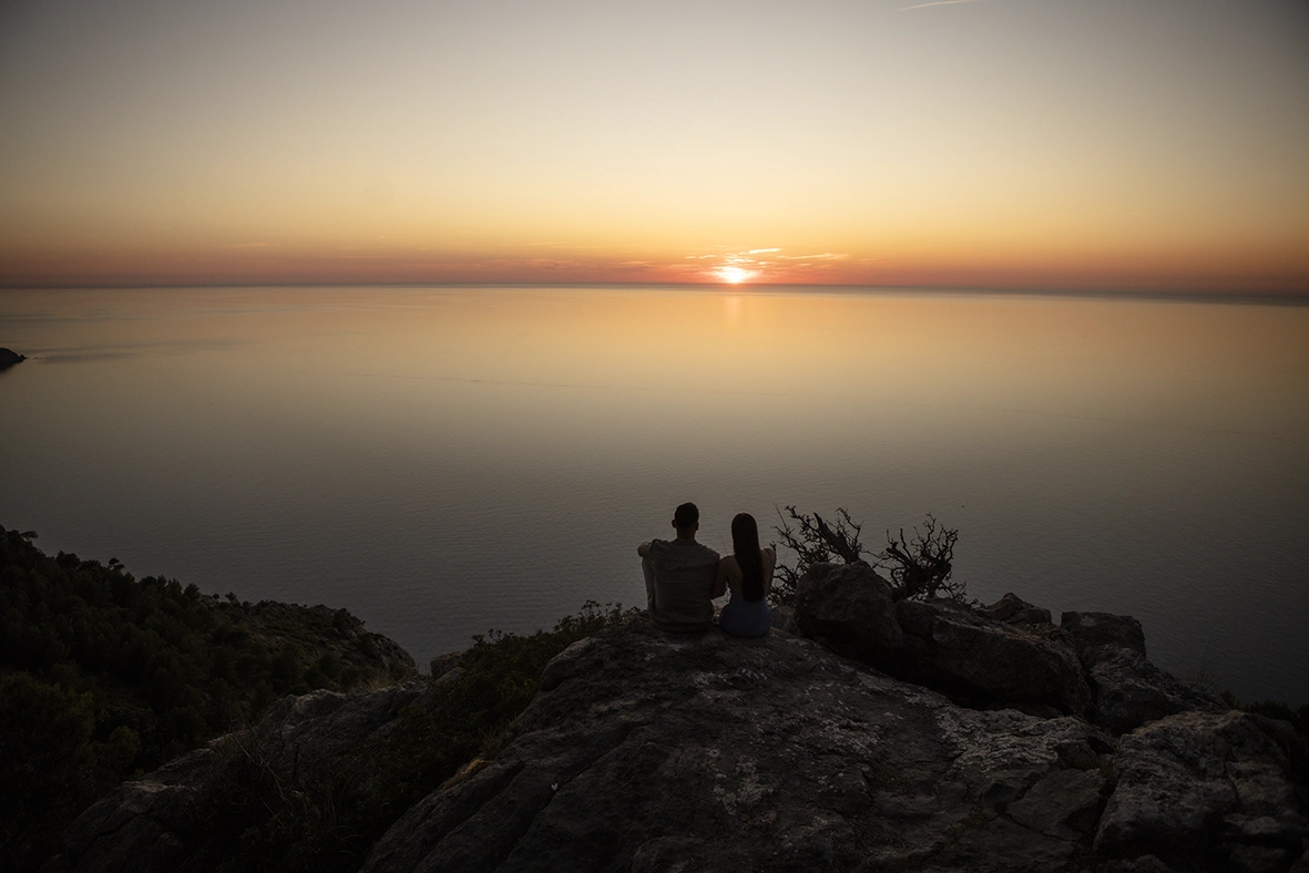 Katie y David contemplan una espectacular puesta de sol sobre el Mediterráneo tras su pedida privada en Mallorca.