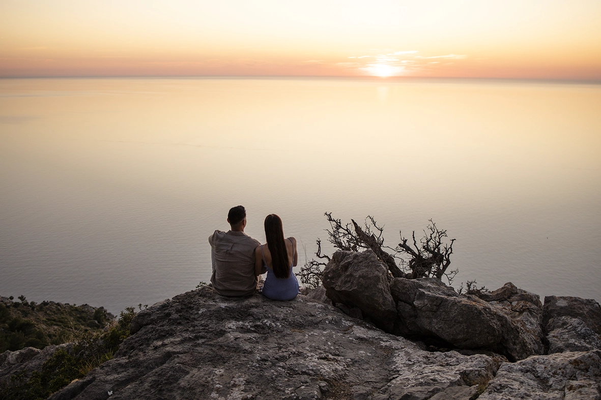 Katie y David contemplan la puesta de sol sobre el Mediterráneo después de su pedida privada en Mallorca.