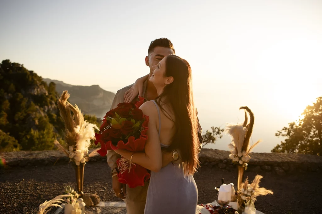 Katie hugging David while holding a bouquet of red roses after their romantic engagement in Mallorca.