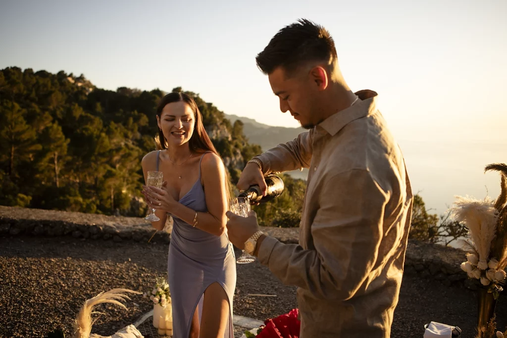 David pouring champagne while Katie smiles during their engagement celebration overlooking the Mediterranean in Mallorca.